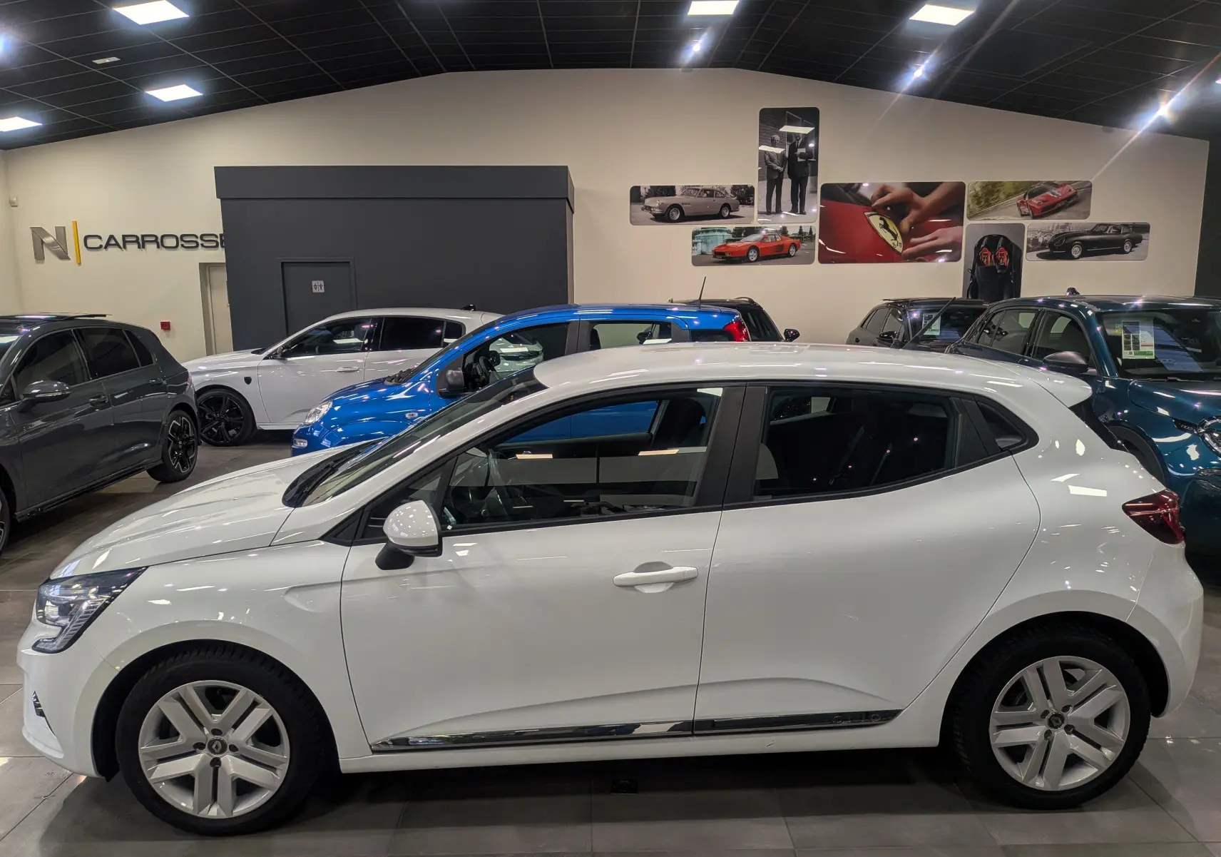 Renault Clio V Blanc Glacier vue de profil côté gauche en intérieur, avec jantes alliage et vitres teintées.