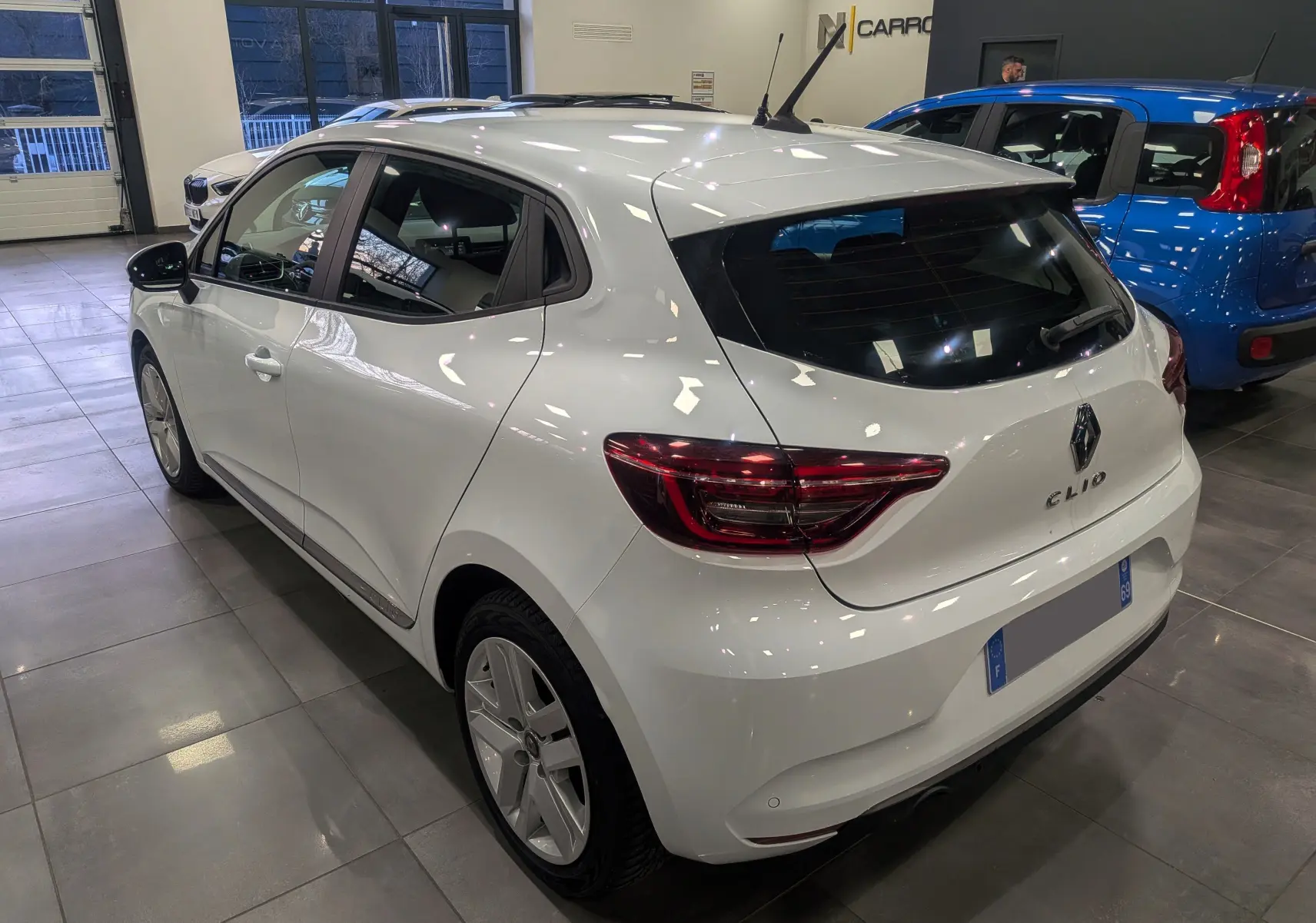 Vue 3/4 arrière droite d'une Renault Clio V blanche Glacier en intérieur, avec feux arrière LED et jantes alliage.