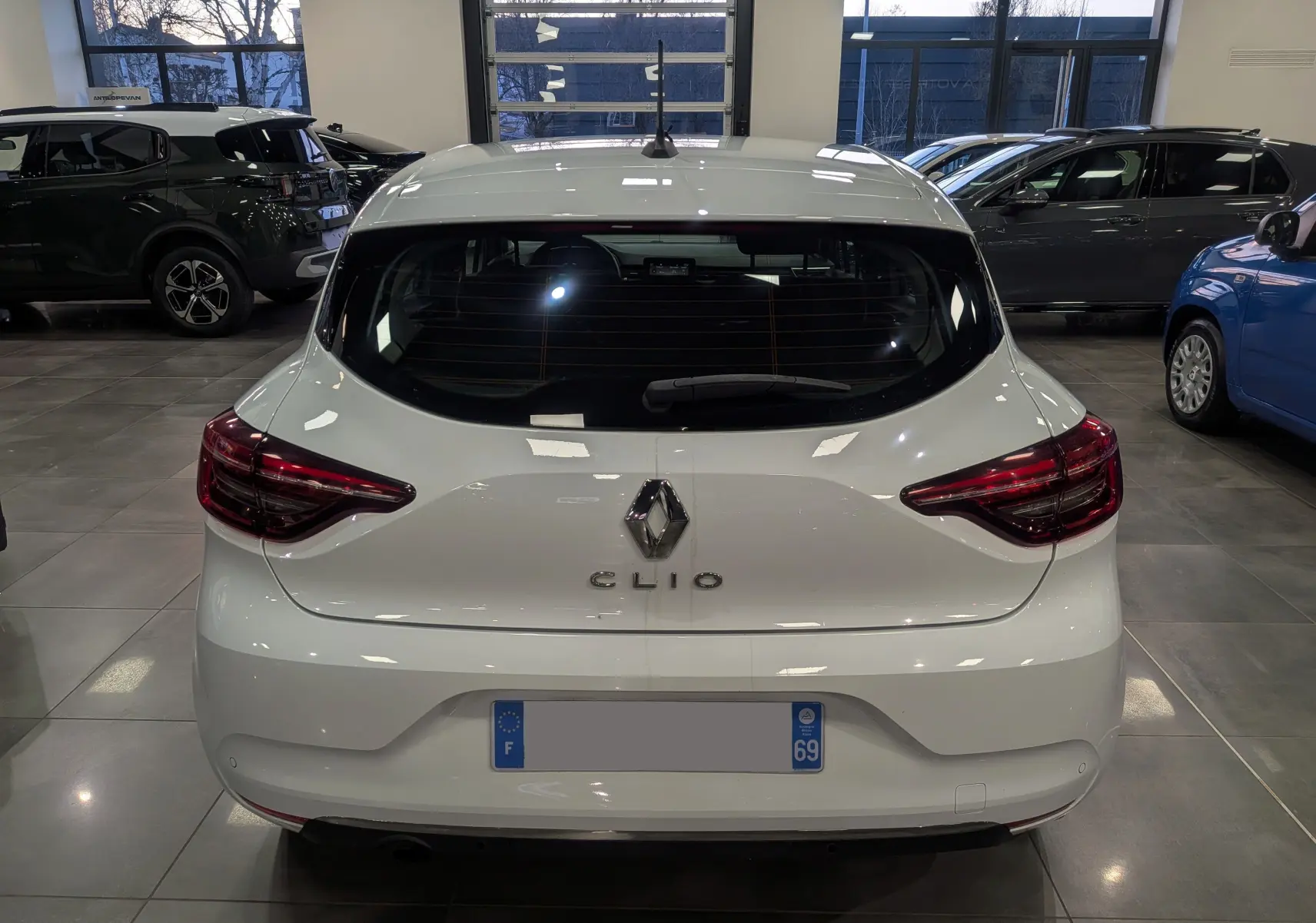 Vue arrière d'une Renault Clio V Blanc Glacier en intérieur, avec feux arrière LED et logo Renault bien visibles.