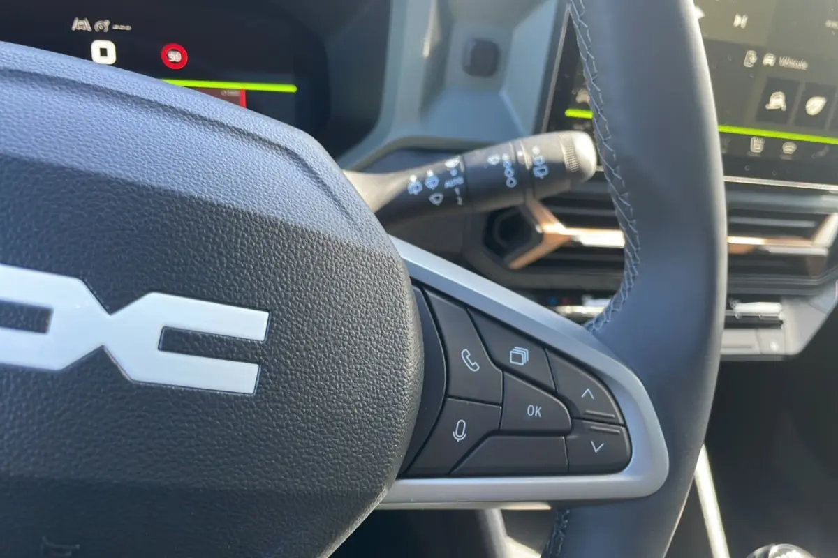 Gros plan sur le volant cuir noir du Dacia Bigster 2025, avec commandes multifonctions et tableau de bord digital en arrière-plan.