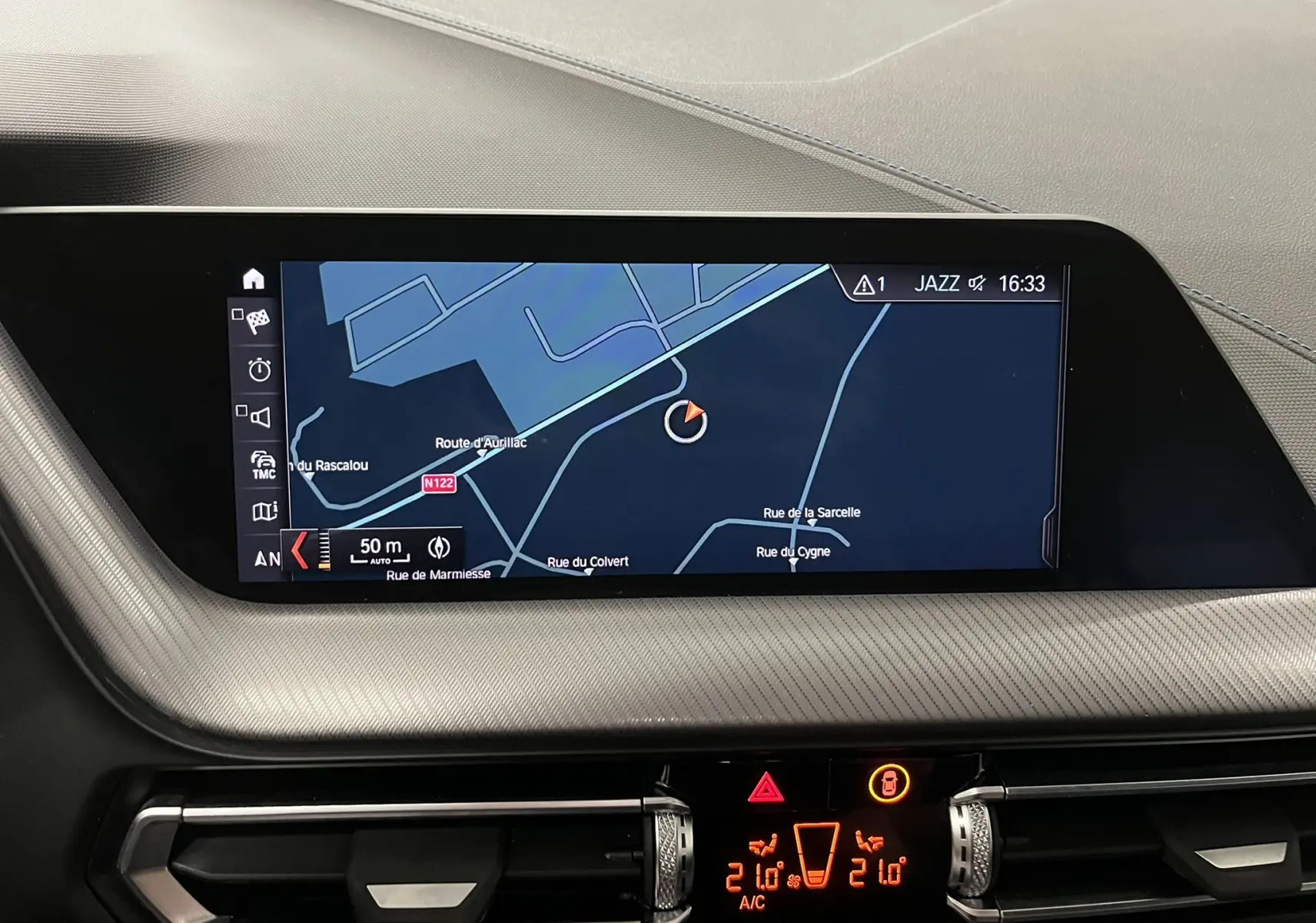 Écran central du tableau de bord BMW Série 1 F40 noir, affichant la navigation GPS et commandes de climatisation digitales.