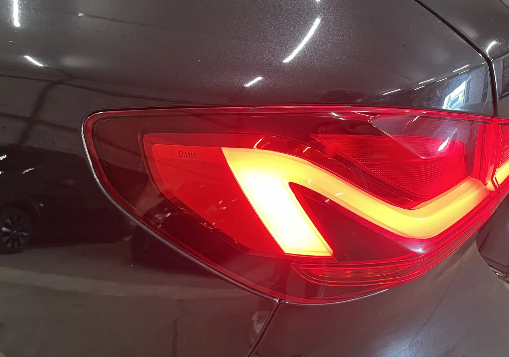Gros plan sur le feu arrière droit allumé d’une BMW Série 1 F40 noire métallisée, soulignant ses lignes LED distinctives.