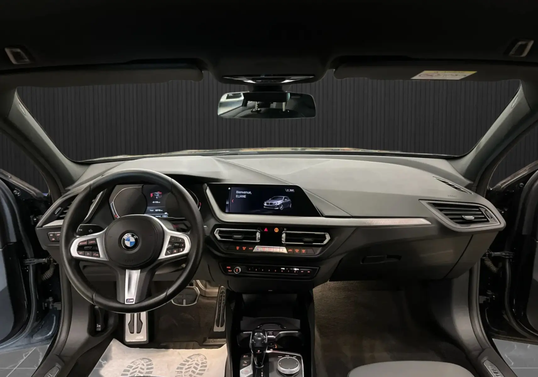Vue intérieure avant de la BMW Série 1 noire, tableau de bord moderne avec écran central et volant sport M.