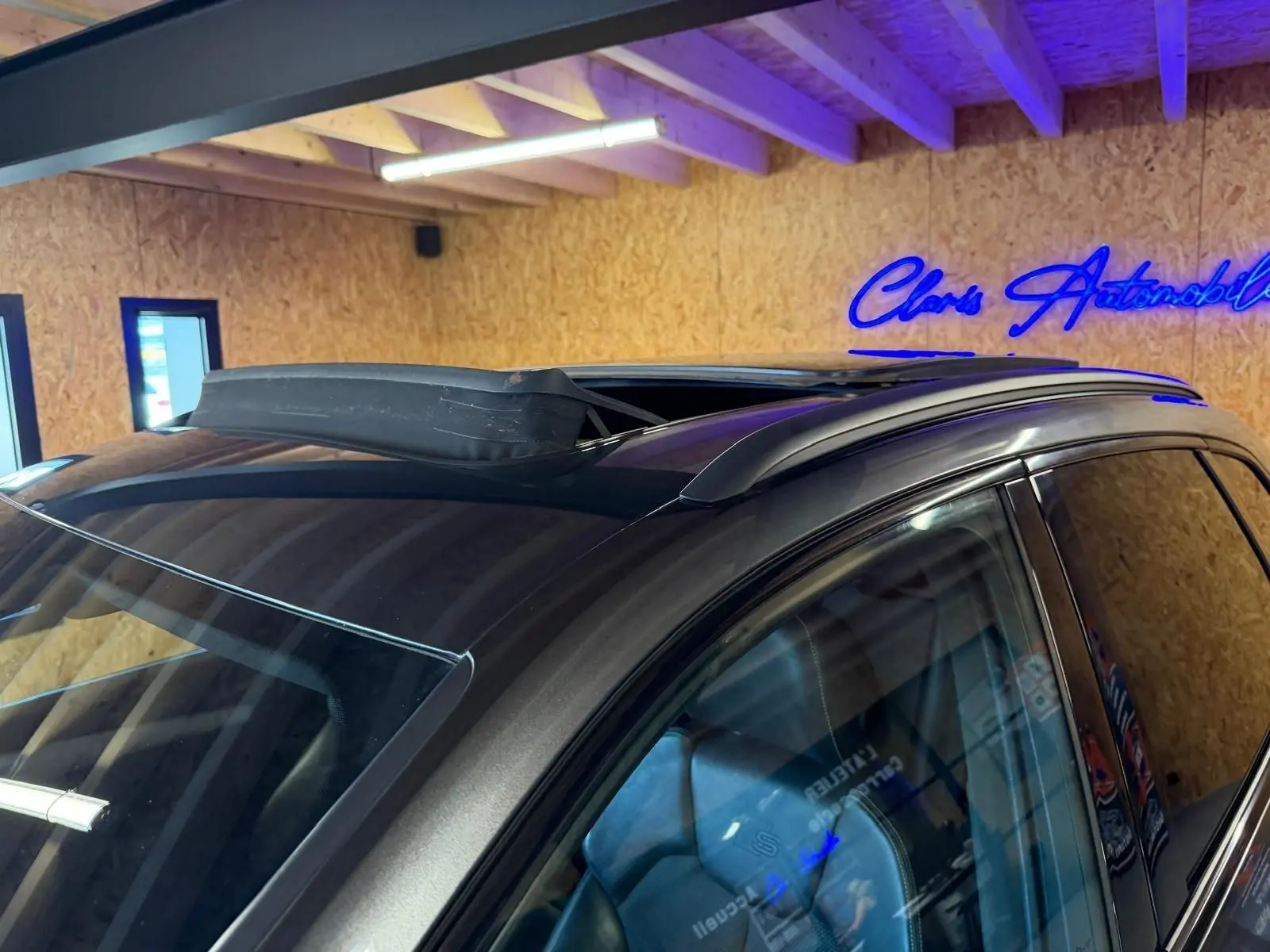 Toit ouvrant ouvert sur le côté gauche d’un Audi Q5 Sportback gris, avec barres de toit visibles en intérieur.