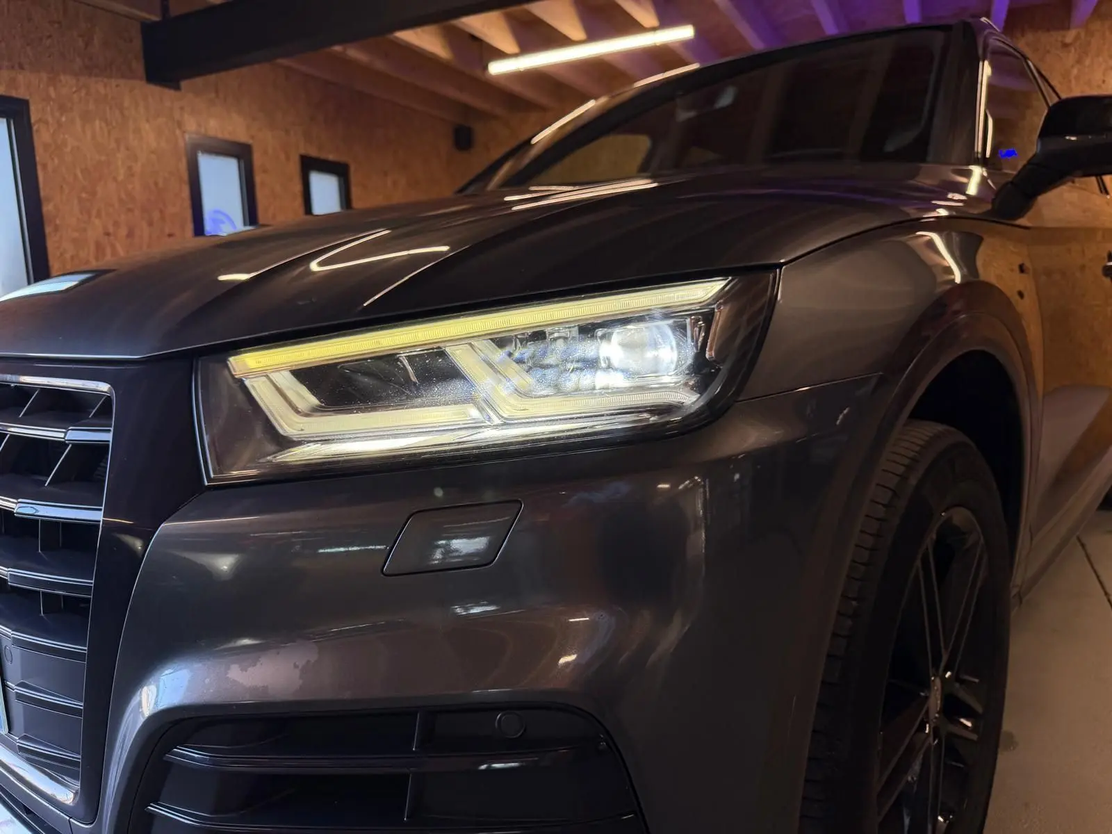 Gros plan sur l'avant droit gris d'un Audi Q5 Sportback 2019 avec phares LED allumés et jante noire visible.