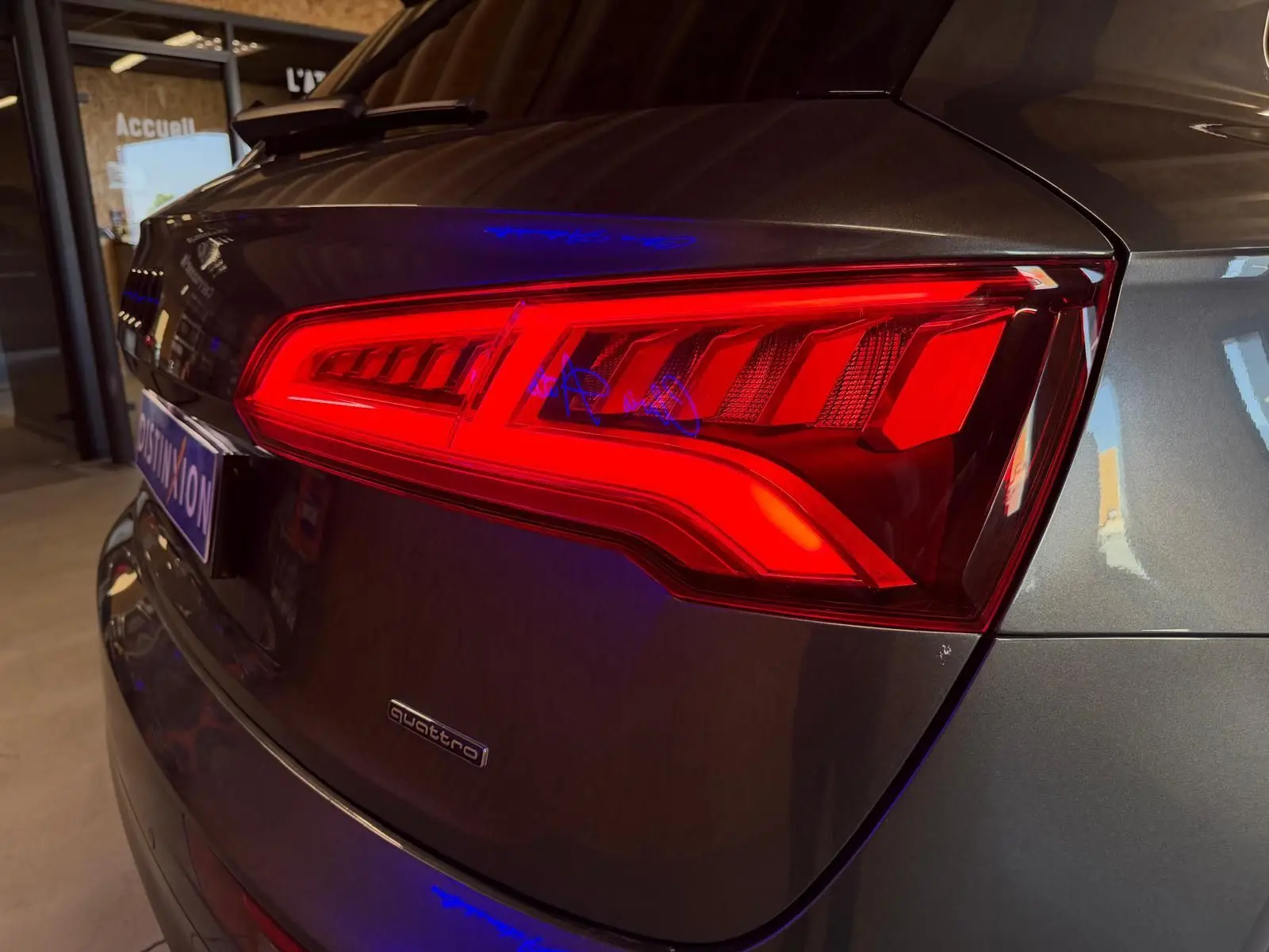 Gros plan sur le feu arrière droit rouge d’un Audi Q5 Sportback gris métallisé, avec logo quattro visible sur le hayon.