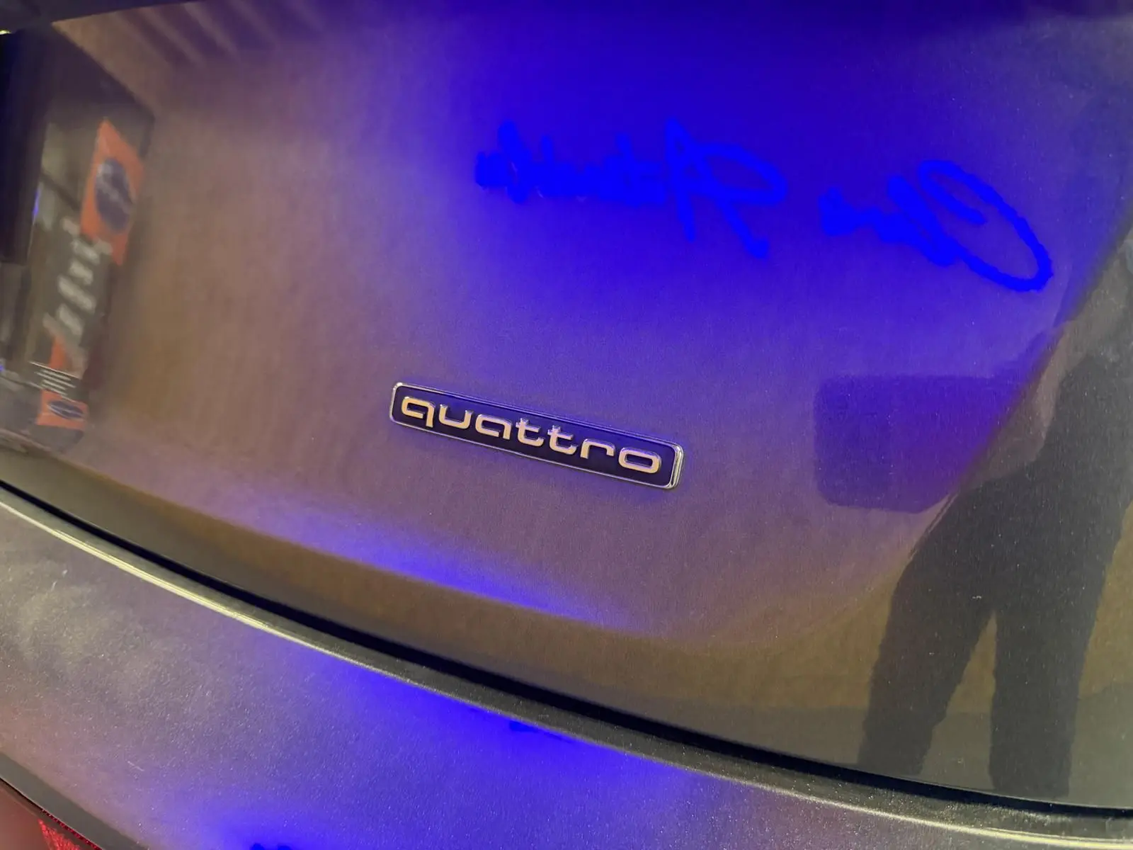 Gros plan sur le logo quattro sur la malle arrière grise d’un Audi Q5 Sportback, reflet bleu visible.