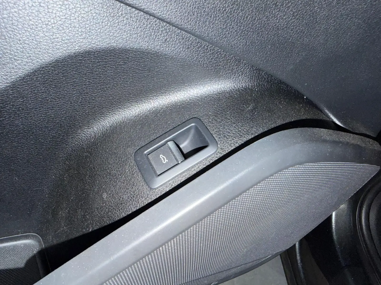 Bouton d'ouverture du hayon intégré dans le panneau intérieur noir côté gauche de l'Audi Q5 Sportback gris.