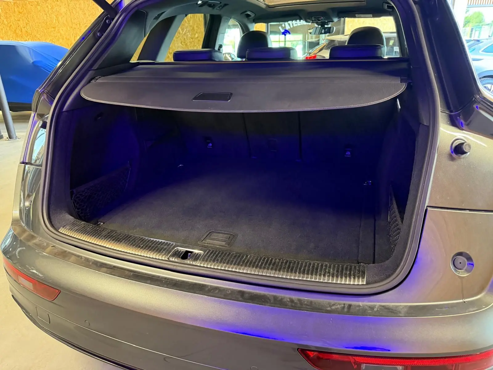 Coffre ouvert vu de l'arrière d'un Audi Q5 Sportback gris 2019, montrant l'espace de chargement vide et la plage arrière.