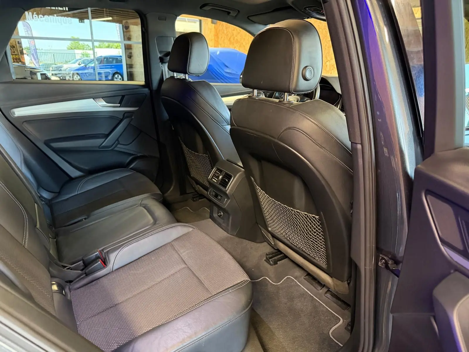 Vue intérieure arrière droite de l’Audi Q5 Sportback gris, sièges en cuir noir avec finitions tissu et rangement filets au dos des sièges avant.