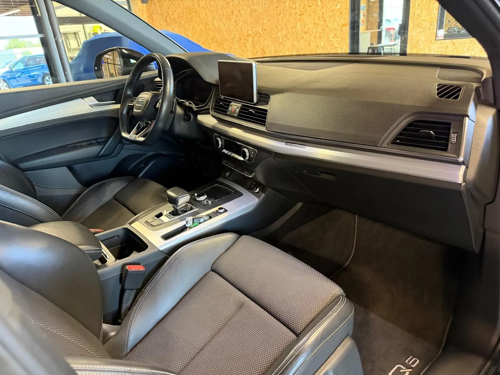 Vue intérieure côté conducteur de l'Audi Q5 Sportback gris, avec tableau de bord moderne et sièges en cuir noir.