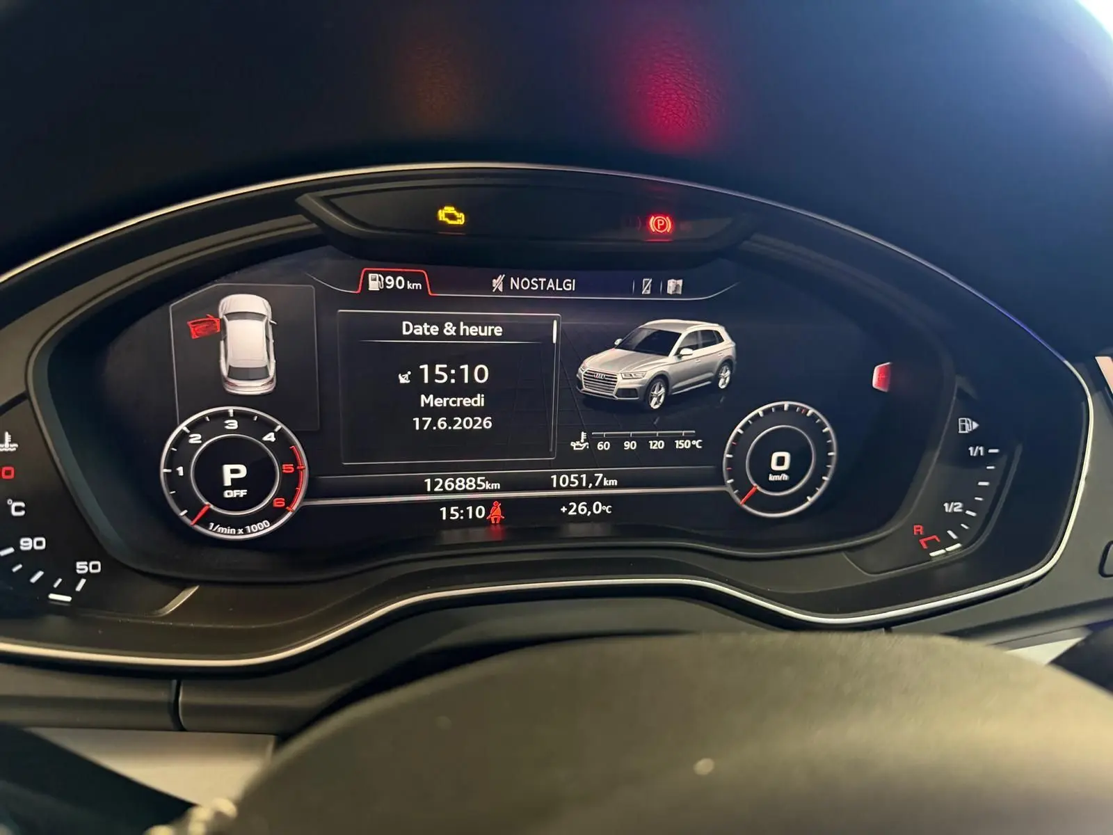 Tableau de bord numérique de l'Audi Q5 gris, affichant la date, l'heure et un véhicule en vue 3/4 avant.
