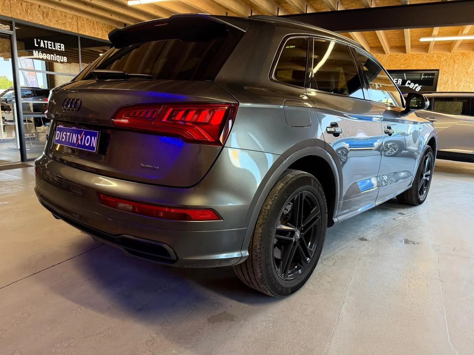 Vue 3/4 arrière droite d'un Audi Q5 Sportback gris métallisé avec jantes noires, stationné en intérieur.