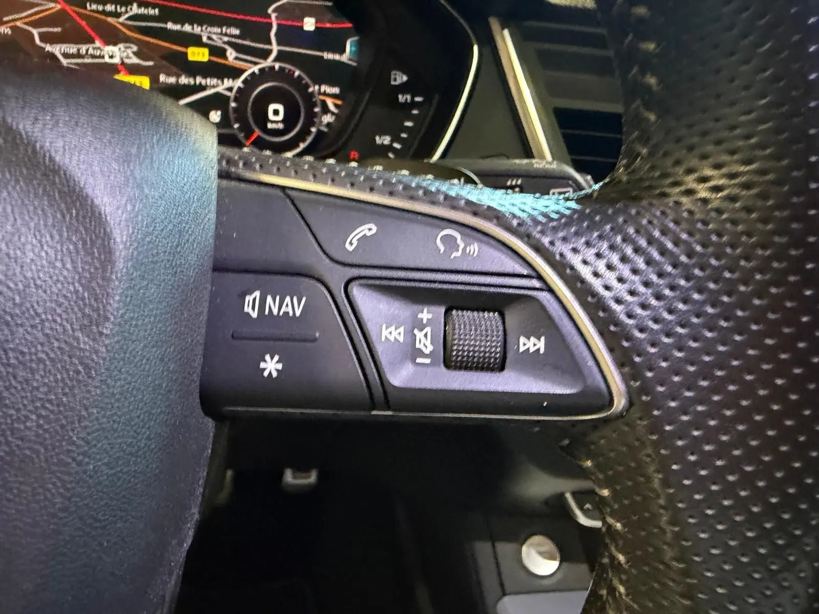 Gros plan sur les commandes du volant côté gauche de l’Audi Q5 Sportback gris, avec affichage numérique en arrière-plan.