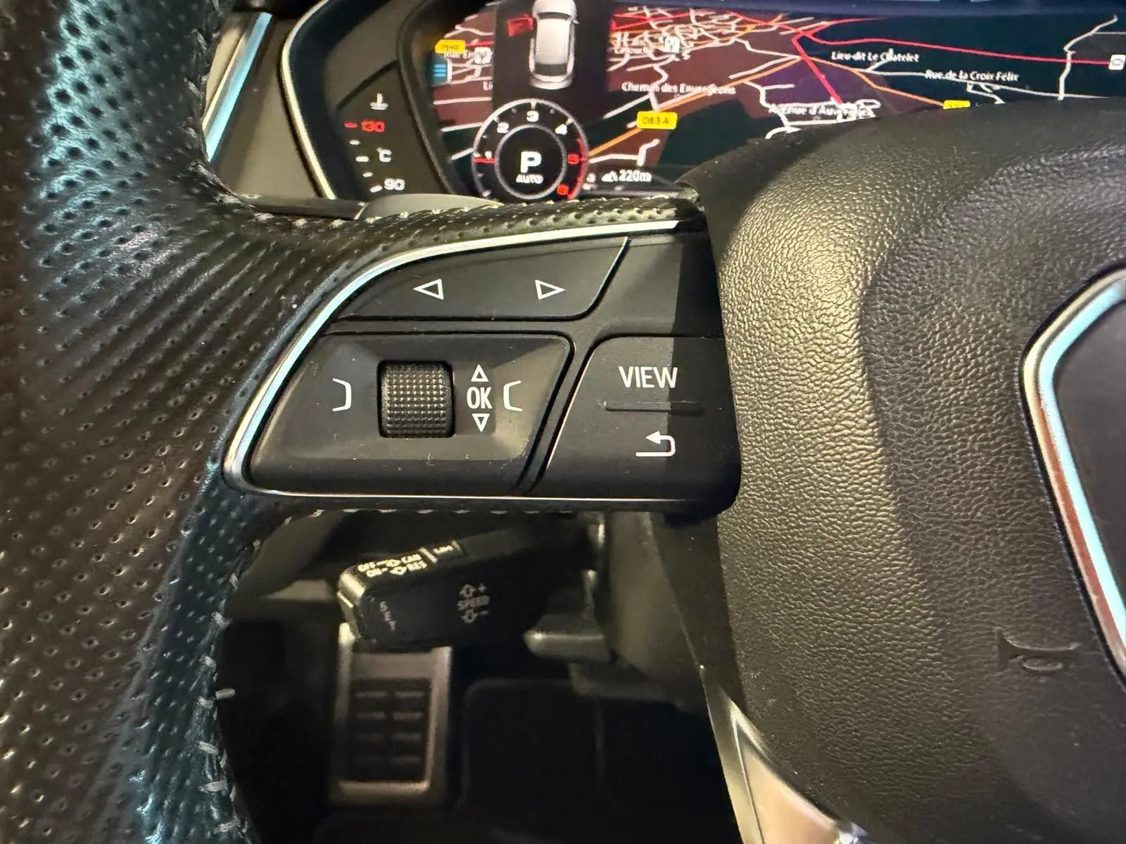 Gros plan sur le volant en cuir perforé de l'Audi Q5 Sportback gris, avec commandes multifonctions et affichage numérique du tableau de bord.