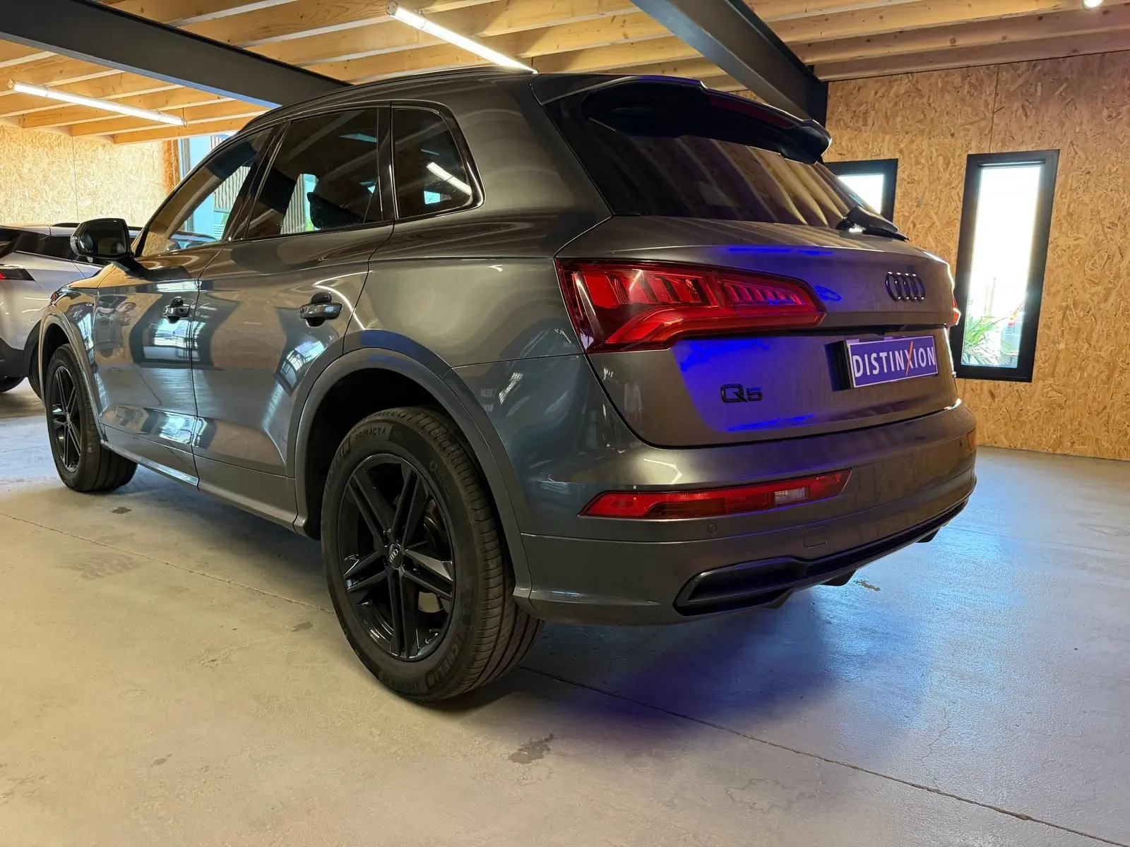 Audi Q5 Sportback gris vue 3/4 arrière droit en intérieur, avec jantes noires et feux arrière allumés.