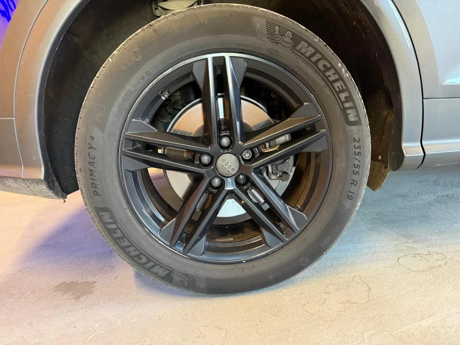 Gros plan sur la roue avant droite d'un Audi Q5 Sportback gris avec jante noire à cinq branches doubles.