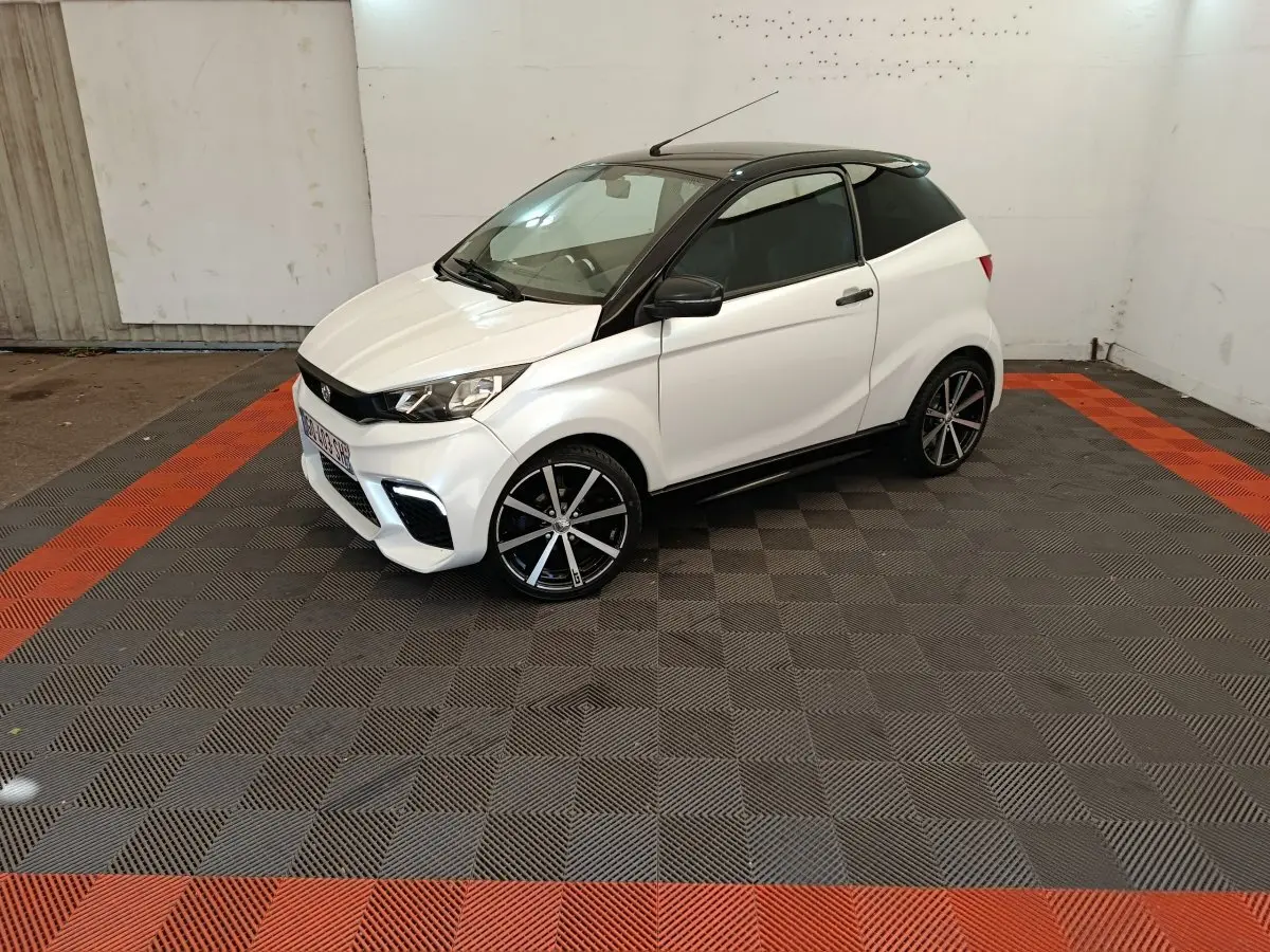 Vue 3/4 avant droite de l'AIXAM AMBITION 0.5 CITY COUPE GTI blanche avec toit noir et jantes alliage noires.
