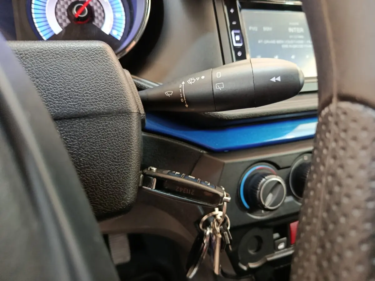 Gros plan sur le volant et la clé de contact d'une Aixam Ambition 0.5 City Coupe GTI 2023, tableau de bord noir et bleu.