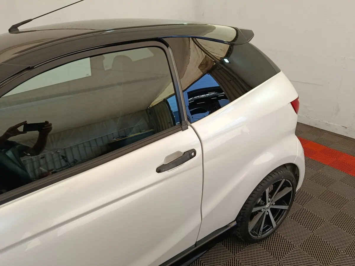 Vue côté gauche arrière d'une Aixam Ambition 0.5 City Coupe GTI blanche avec toit noir et jante alliage noire.