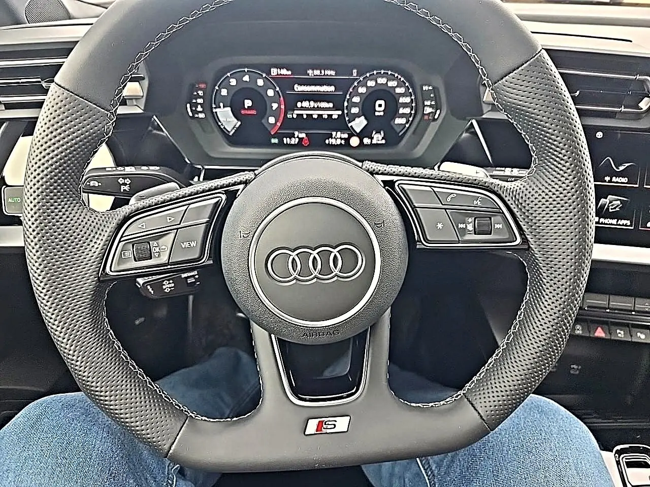 Vue rapprochée du volant sport en cuir noir perforé avec logo S d'une Audi A3 Sportback 2026, tableau de bord digital visible.