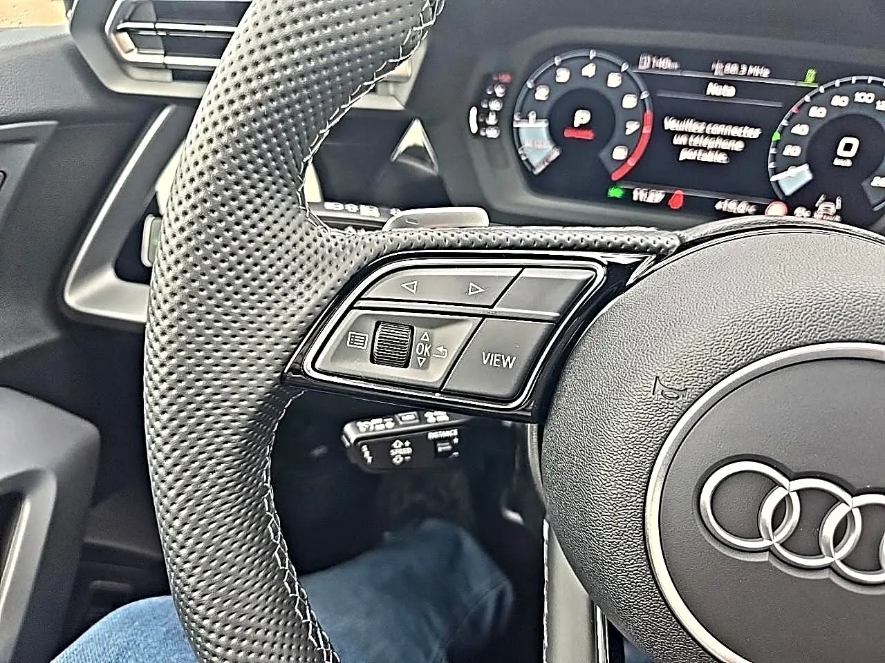Gros plan sur le volant cuir perforé côté gauche de l’Audi A3 Sportback 2026 avec commandes multifonctions et tableau de bord digital.
