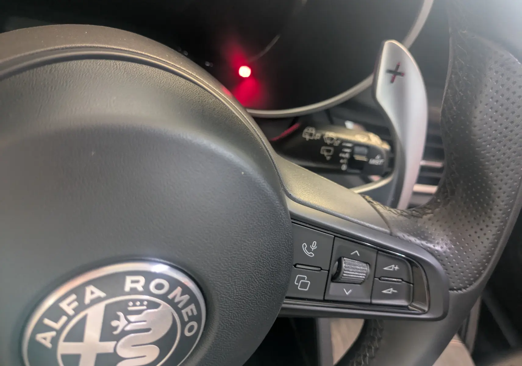 Gros plan sur le volant en cuir perforé de l'Alfa Romeo Stelvio blanc, avec commandes intégrées et palette de vitesse + visible.