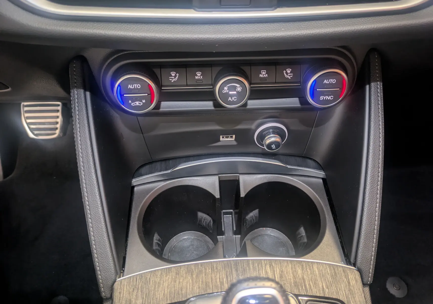 Gros plan sur la console centrale de l'Alfa Romeo Stelvio blanc, avec commandes de climatisation et porte-gobelets visibles.