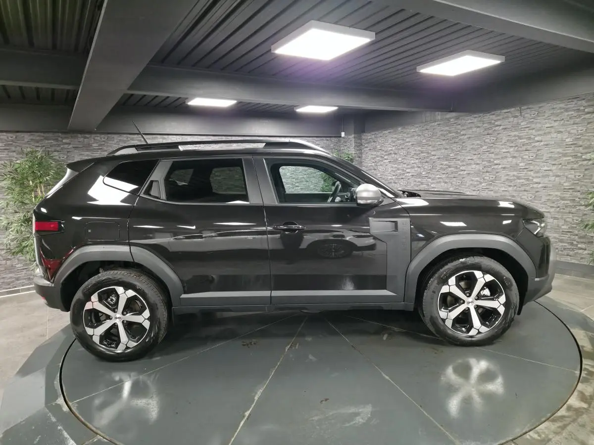 Profil droit du Dacia Duster 1.6 Hybrid 2025 noir nacré avec jantes alliage diamantées et barres de toit noires.