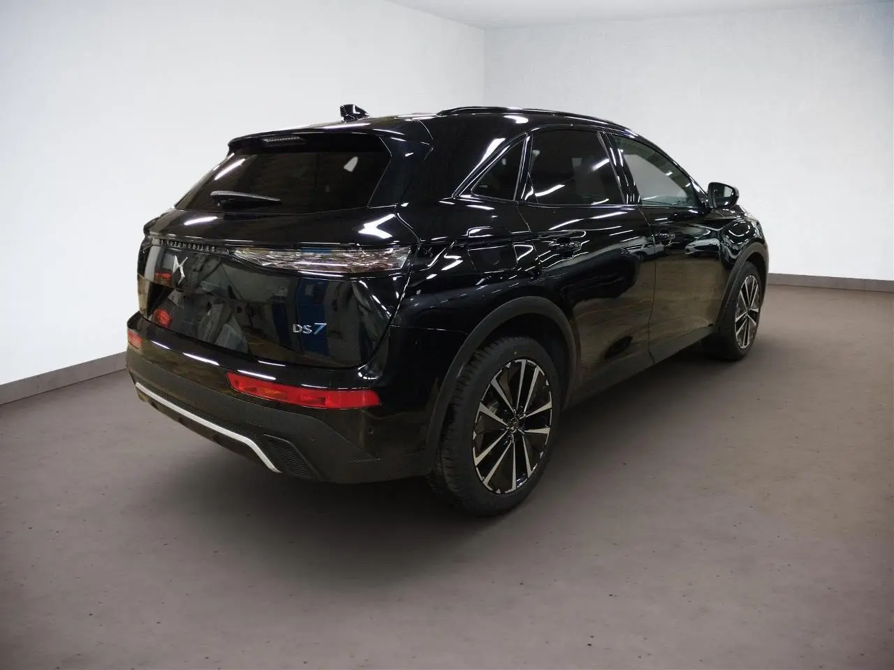 Vue 3/4 arrière droite d'un DS7 noir Perla avec jantes alliage et feux arrière LED 3D dans un intérieur neutre.