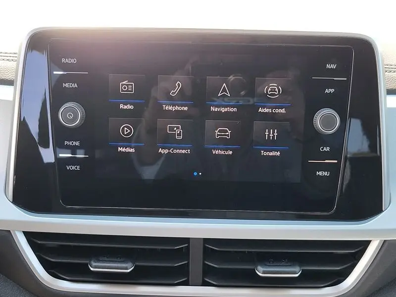 Écran tactile central du Volkswagen T-Roc 2025 gris Indium, affichant le menu principal avec options radio, téléphone et navigation.