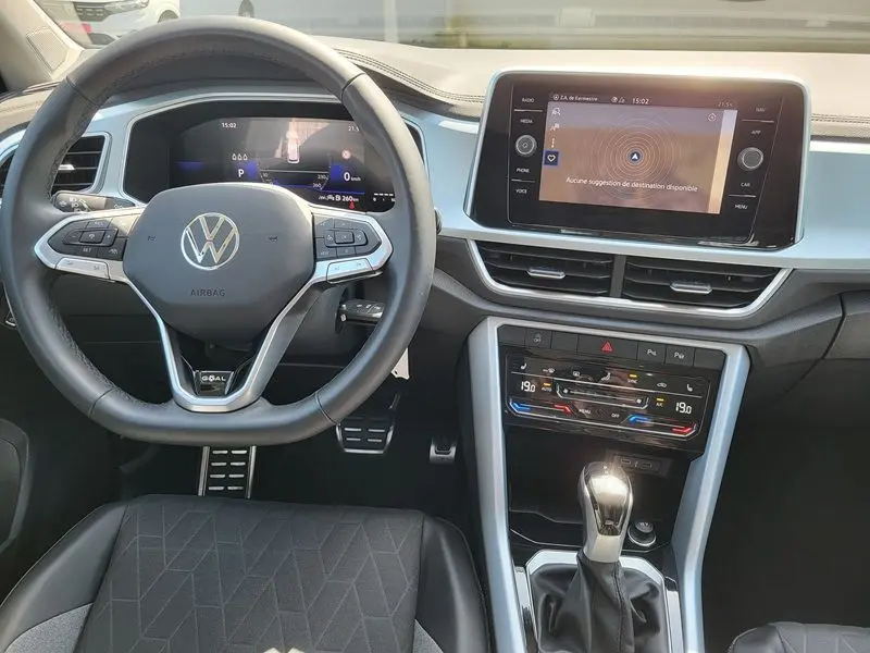 Vue intérieure du tableau de bord et volant du Volkswagen T-Roc gris Indium 2025 avec écran tactile et commandes au volant.