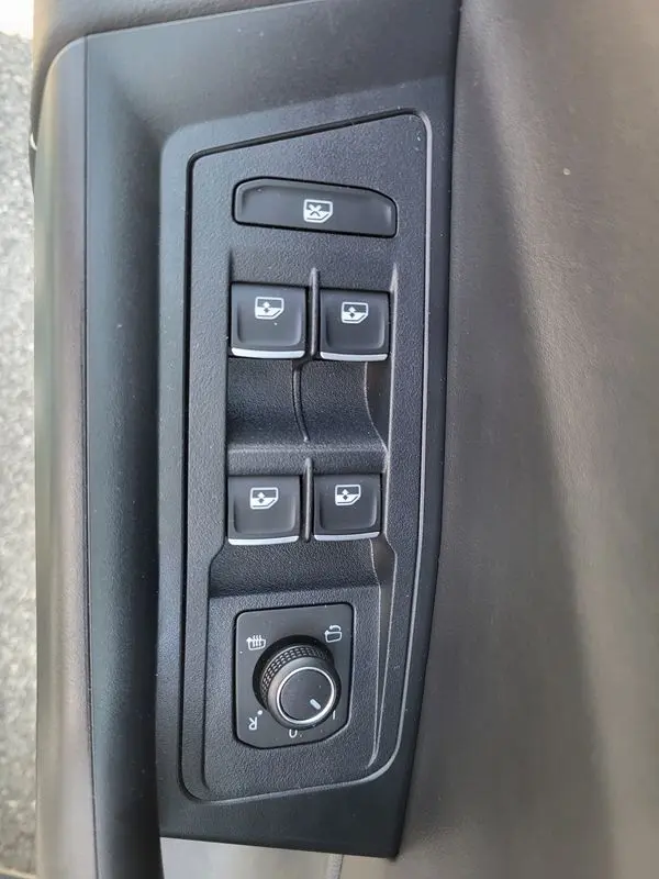 Vue rapprochée des commandes de lève-vitres et réglage des rétroviseurs côté conducteur du Volkswagen T-Roc gris Indium 2025.