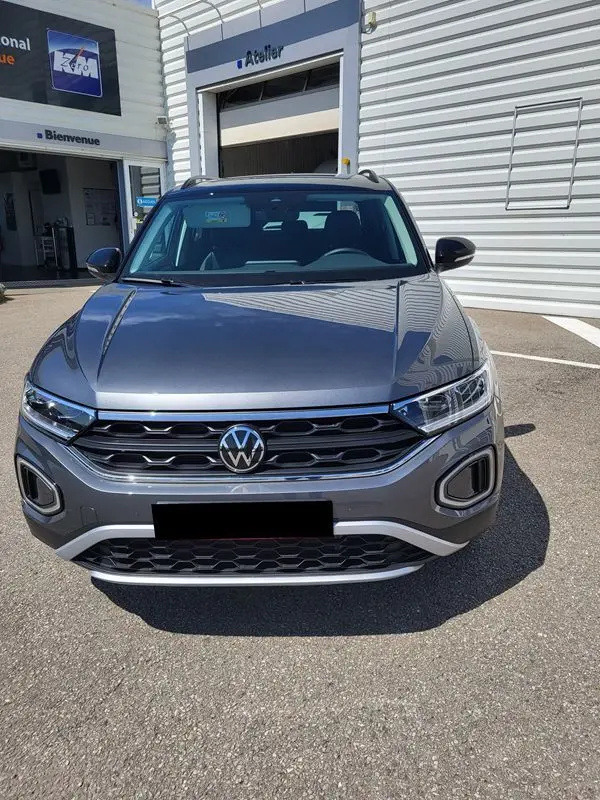 Vue avant d'un Volkswagen T-Roc gris Indium 2025, mettant en valeur la calandre chromée et les phares LED distinctifs.