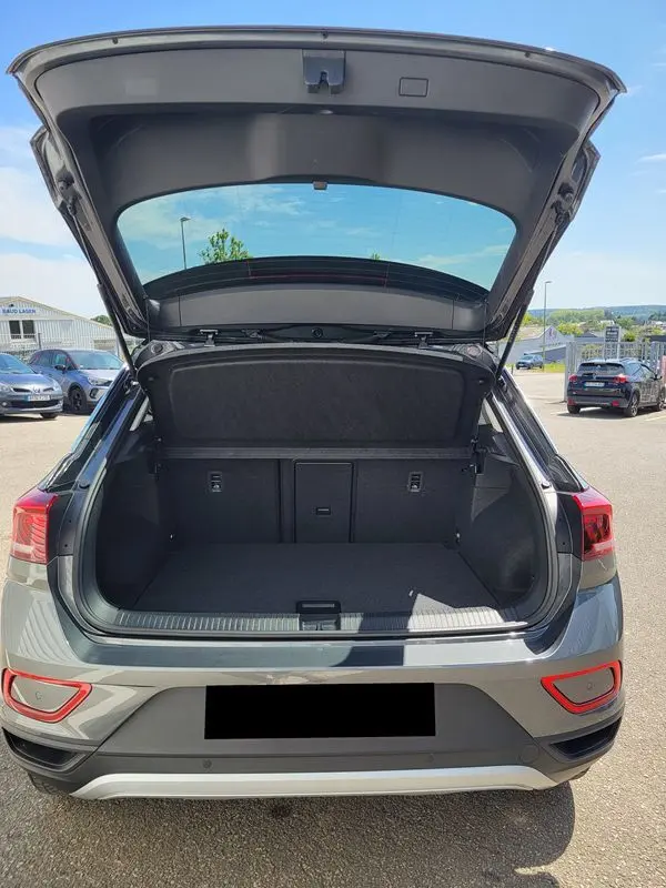Vue arrière du Volkswagen T-Roc gris Indium 2025 avec coffre ouvert, montrant l'espace de chargement vide et l'attelage amovible.
