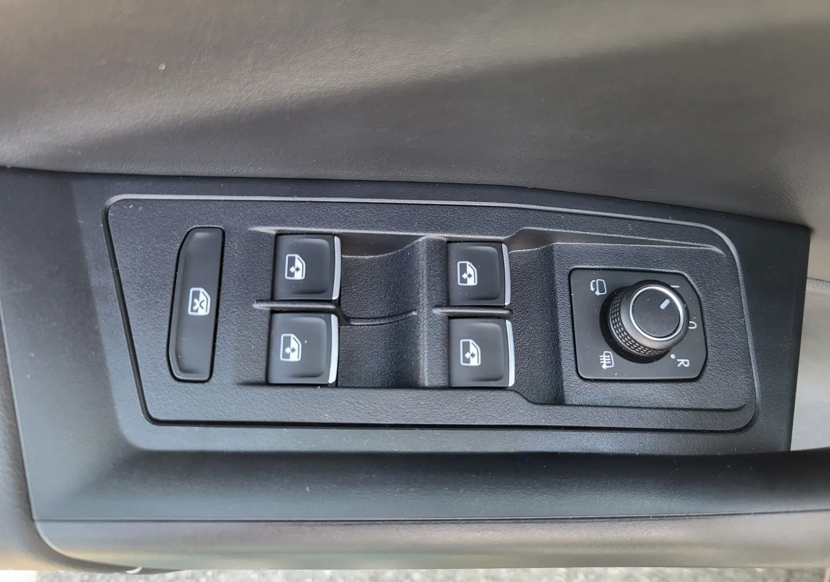 Gros plan sur les commandes de lève-vitres et réglage des rétroviseurs côté conducteur du Volkswagen T-Roc gris Indium 2025.