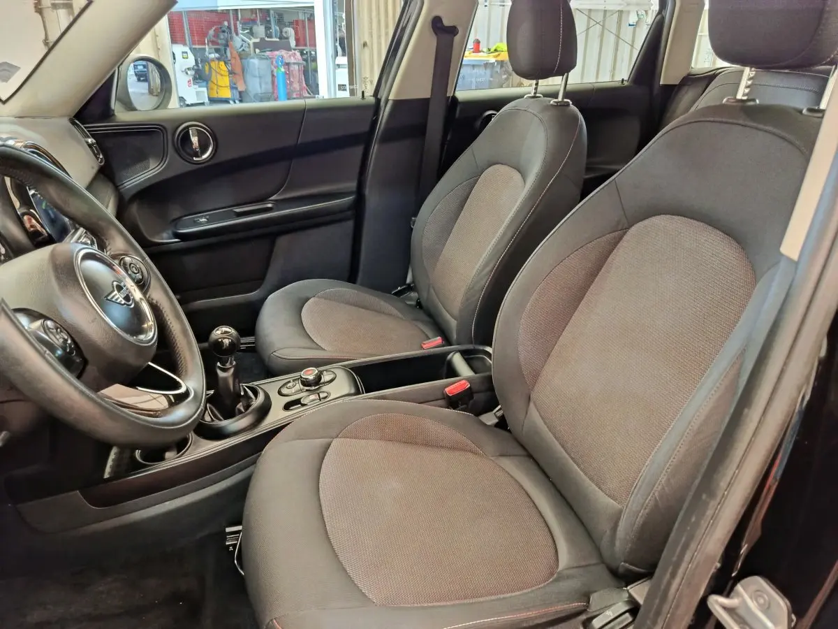 Vue intérieure côté conducteur de la MINI Countryman noire 2019, sièges tissu gris et volant cuir multifonctions.