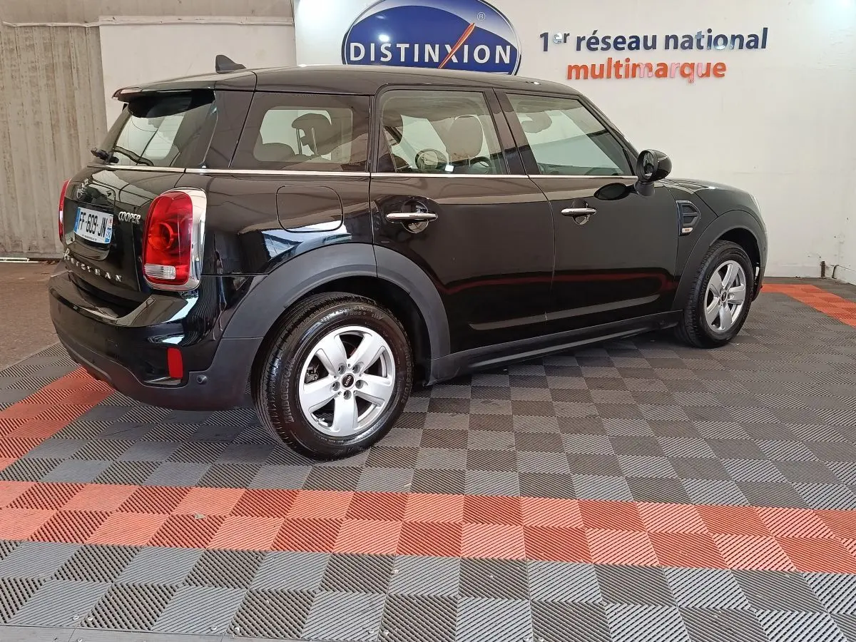 Vue 3/4 arrière droit d'une MINI Countryman noire stationnée en intérieur, avec jantes argentées et logo Cooper visible.