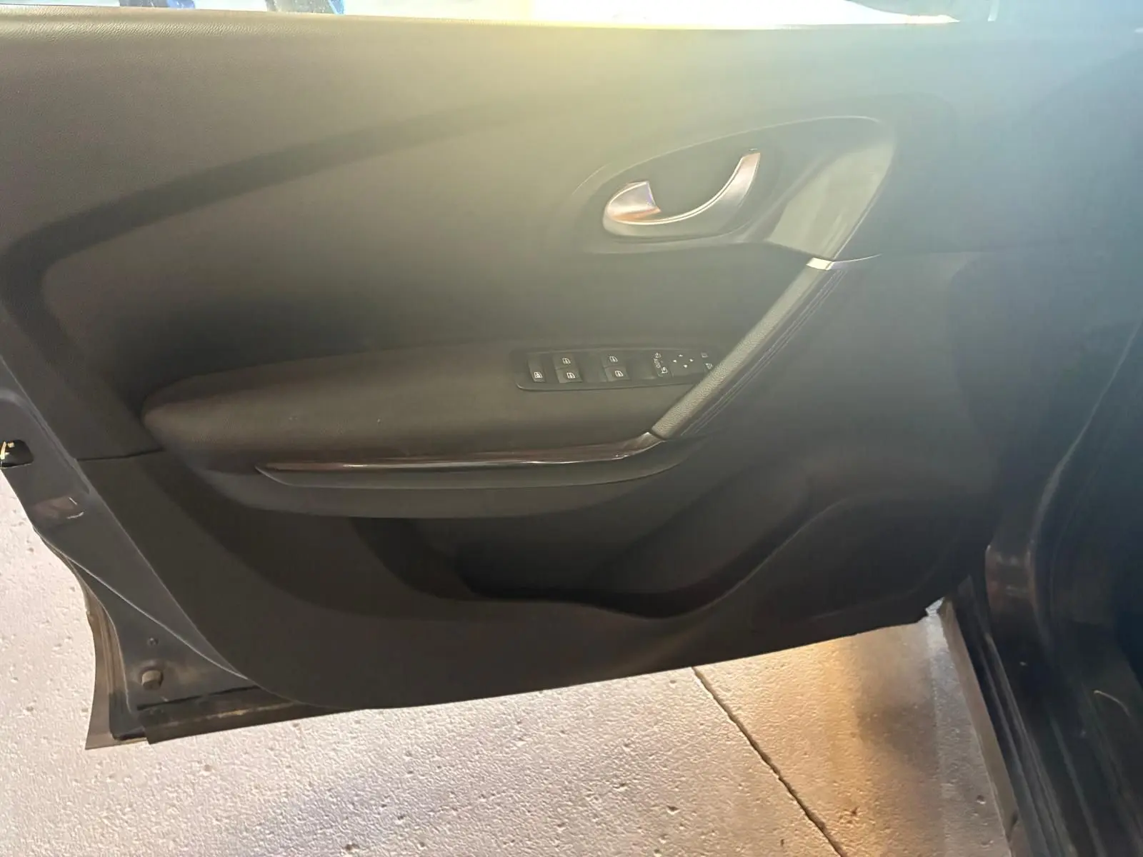 Vue intérieure côté gauche de la porte avant d’un Renault Kadjar gris avec commandes de vitres et poignée argentée.