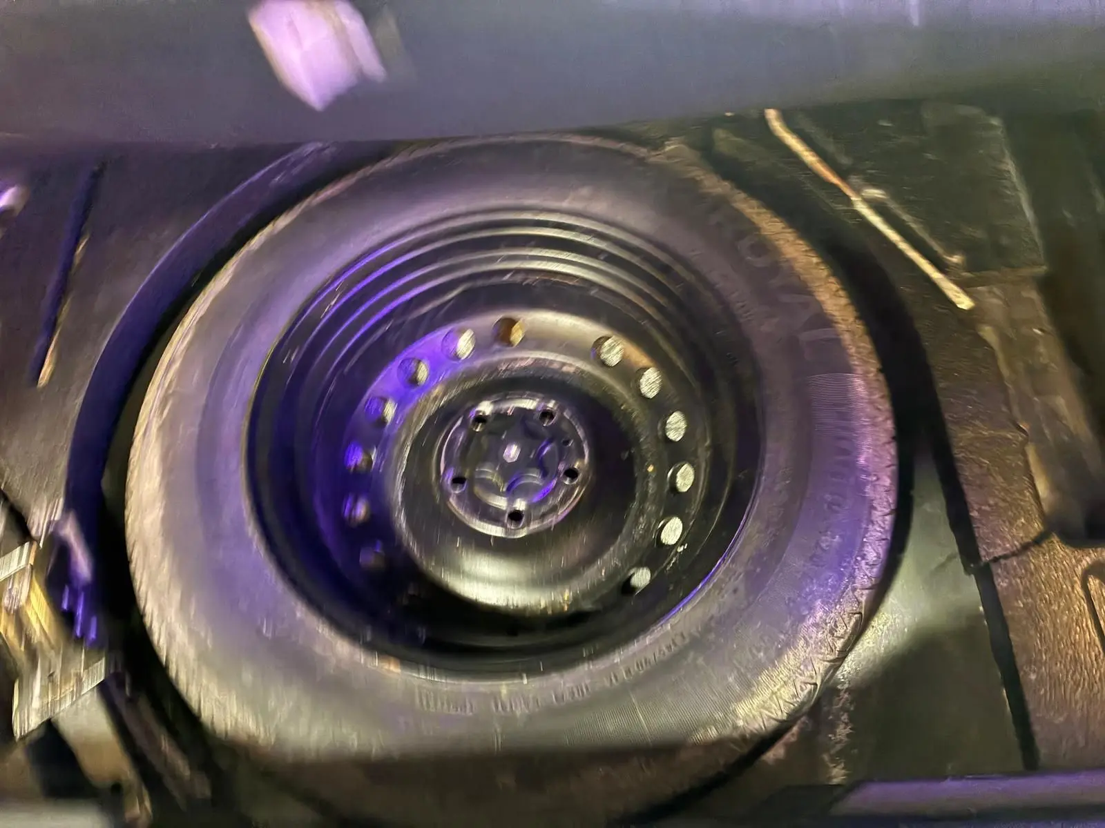Roue de secours noire dans le coffre d'un Renault Kadjar gris, vue en plongée sur le pneu et la jante acier.