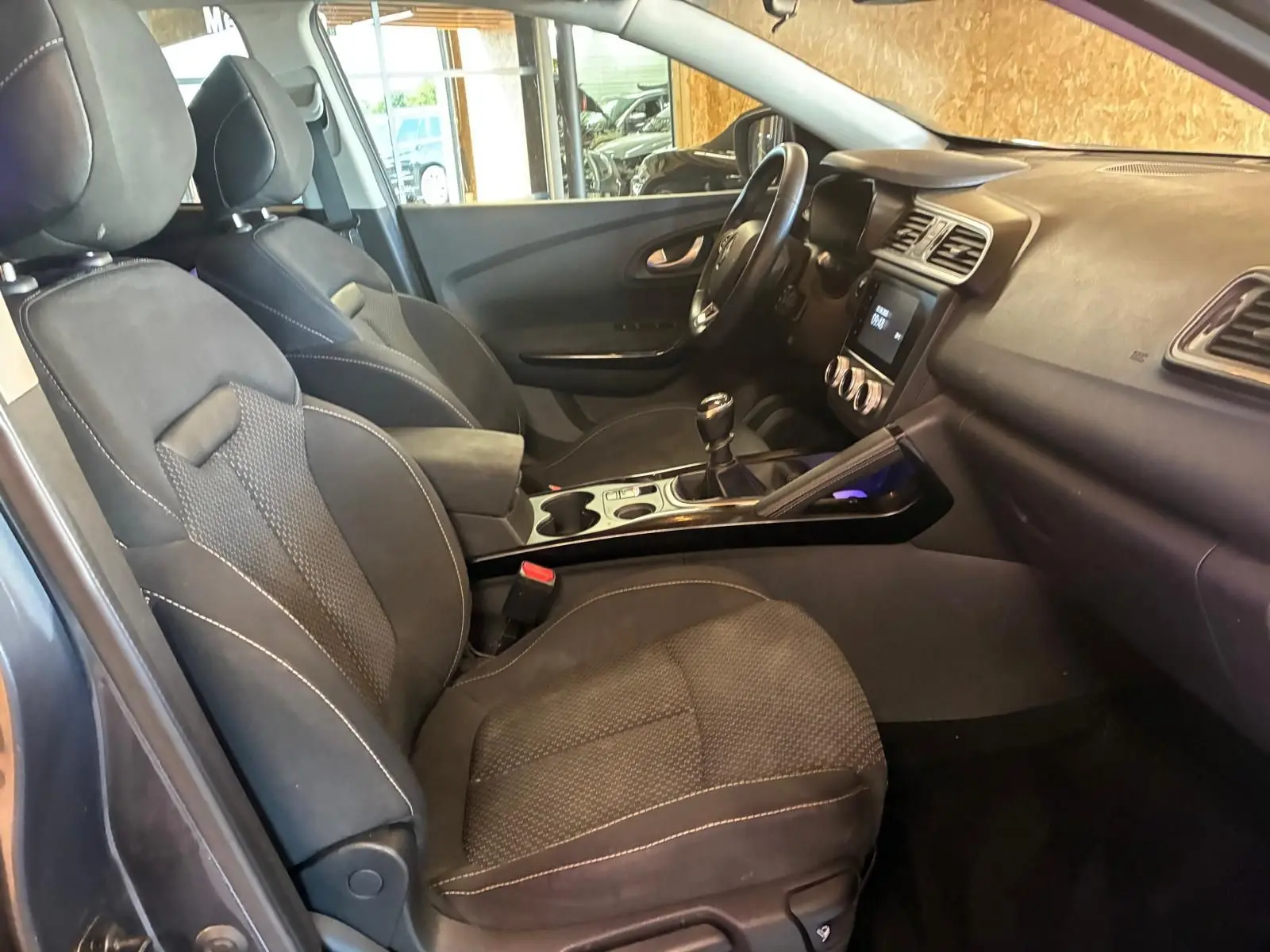 Vue intérieure côté conducteur du Renault Kadjar 2019, sièges tissu noir et tableau de bord avec écran tactile.