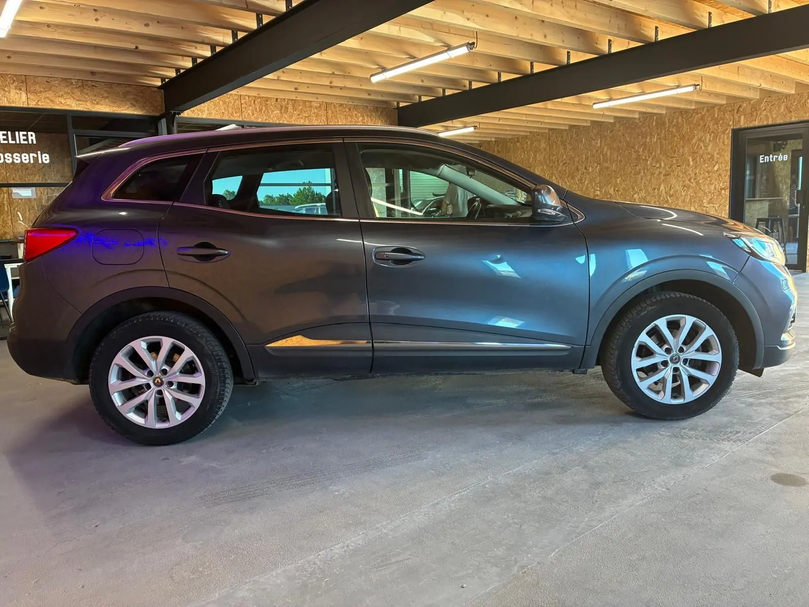 Vue de profil côté gauche d'un Renault Kadjar gris 2019 stationné en intérieur avec jantes alliage visibles.
