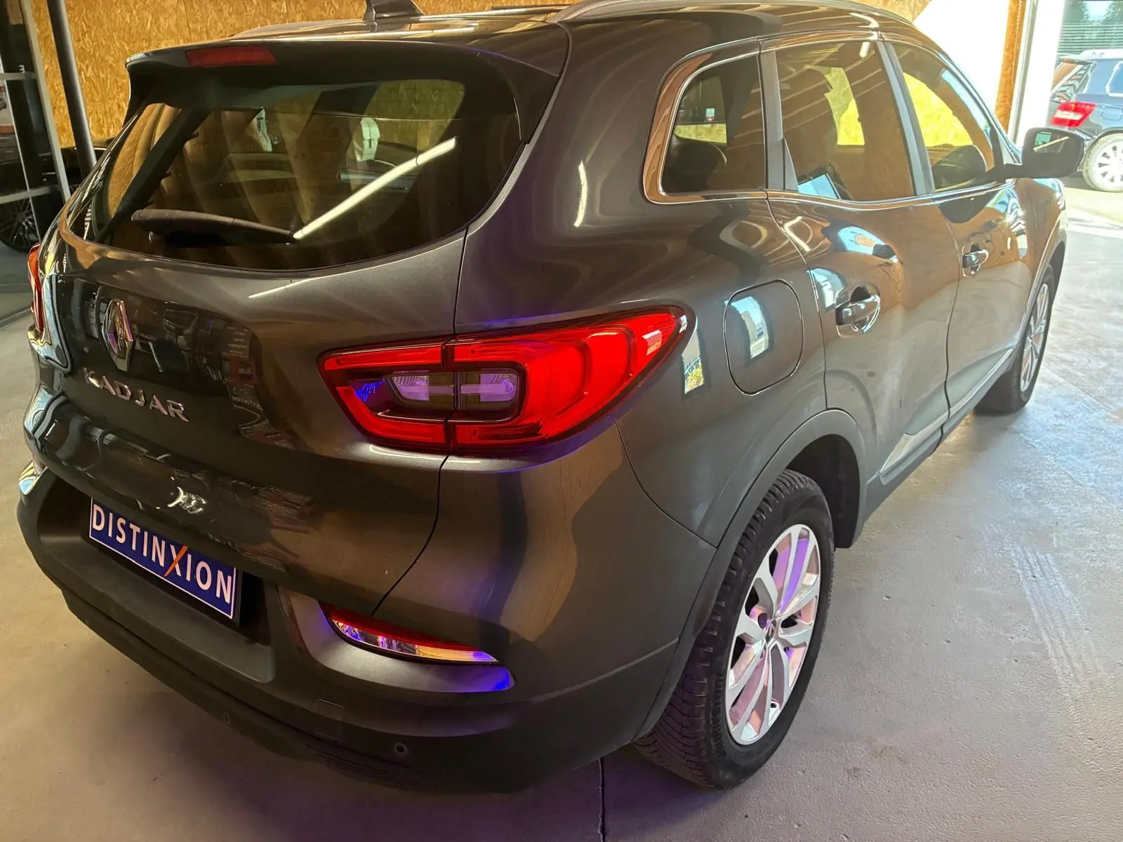 Vue 3/4 arrière droit d'un Renault Kadjar gris métallisé garé en intérieur avec feux arrière allumés.