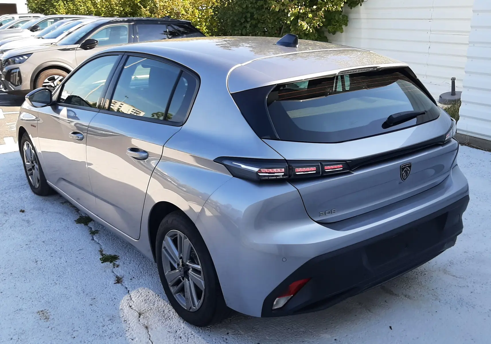 Vue 3/4 arrière droite d'une Peugeot 308 III Hybrid gris Artense avec feux arrière LED distinctifs, stationnée en extérieur.