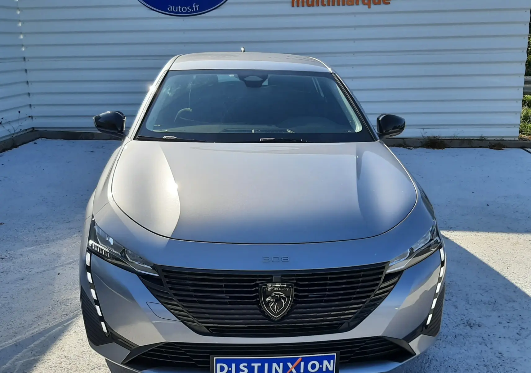Vue avant d'une Peugeot 308 III Hybrid gris Artense avec calandre noire et feux LED verticaux allumés.