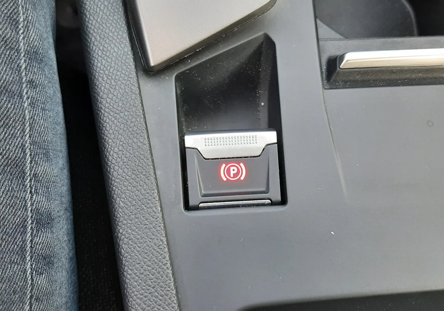 Gros plan sur le bouton de frein à main électrique rouge dans la console centrale noire d’une Peugeot 308 III Hybrid 2025.