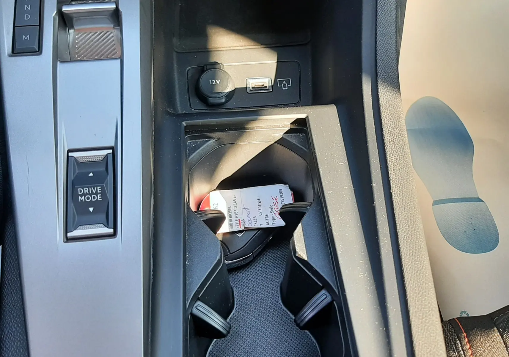 Vue rapprochée de la console centrale noire de la Peugeot 308 gris Artense avec porte-gobelets et commandes de boîte auto.