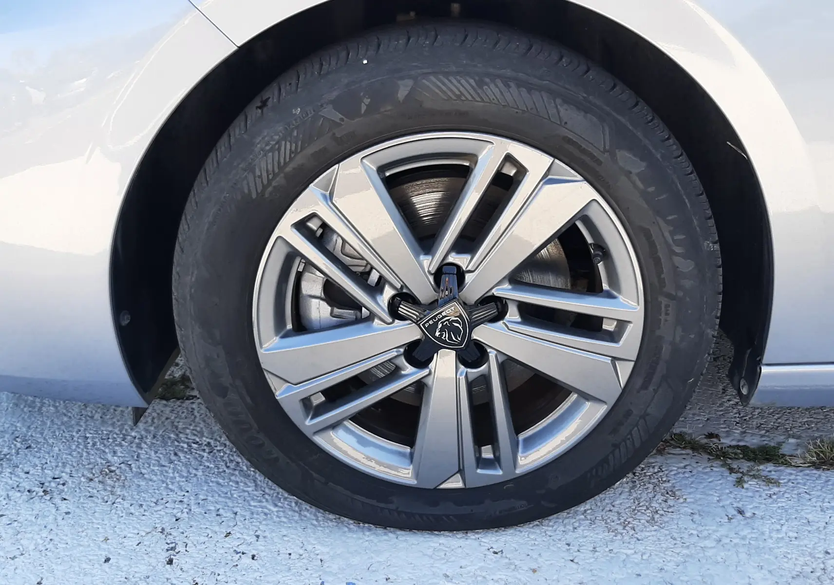 Gros plan sur la roue avant droite d’une Peugeot 308 gris Artense avec jante alliage et logo lion au centre.