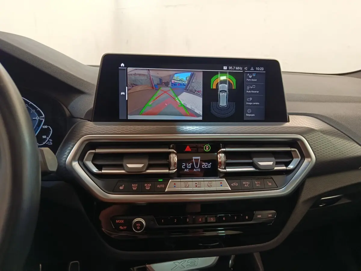 Vue intérieure du tableau de bord du BMW X3 blanc 2023 avec écran tactile affichant l'aide au stationnement.