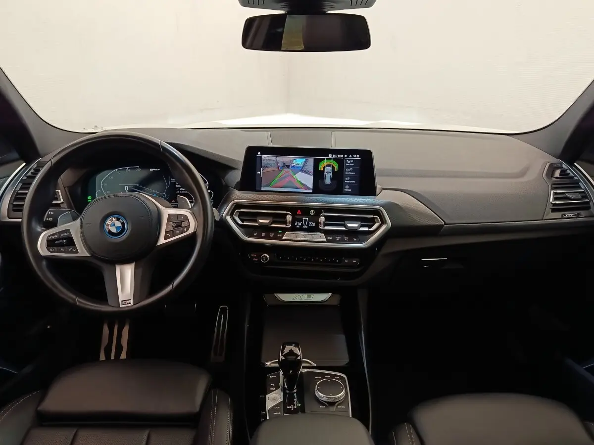 Vue intérieure avant du tableau de bord noir du BMW X3 xDrive30e avec écran tactile central et volant multifonction.
